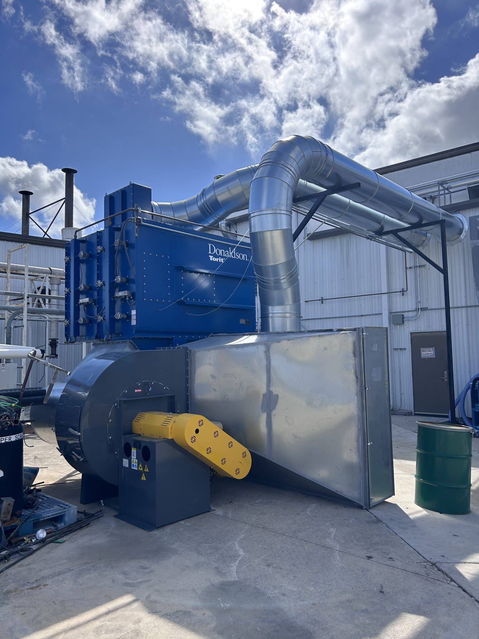 Large blue Donaldson Torit centralized dust collector with a heavy-duty blower and large silver ductwork installed outside an industrial facility